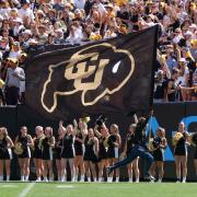 Student runs down sideline with a giant CU flag during a football game